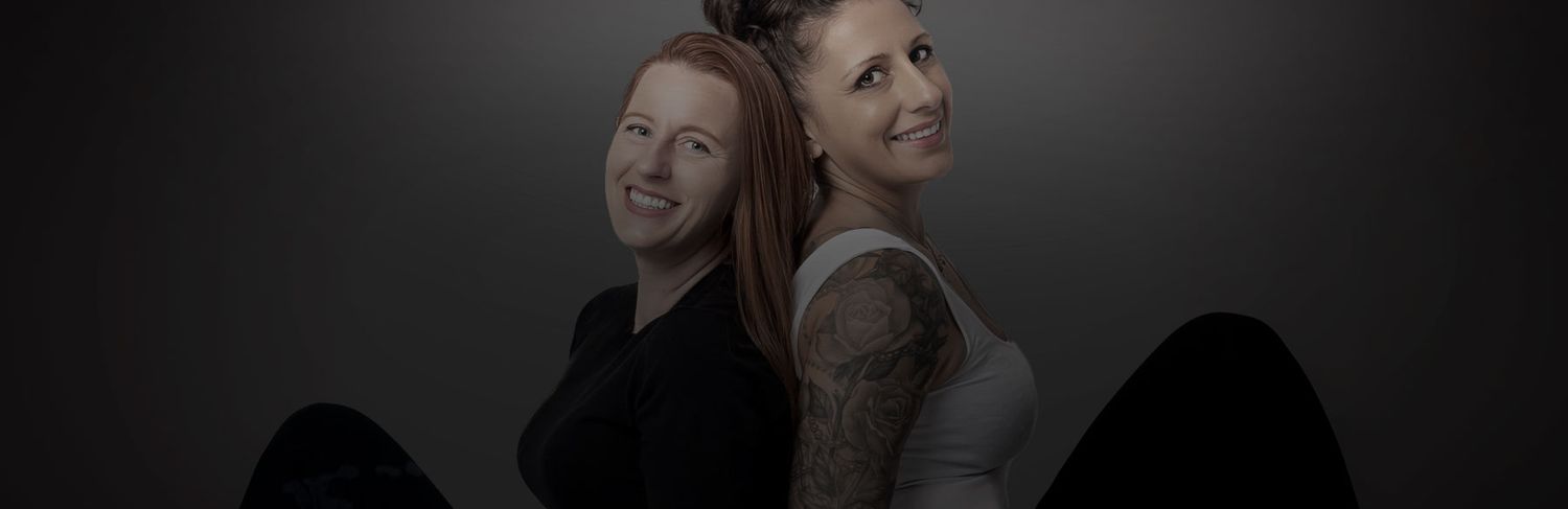 Two women posing back-to-back against a dark gray studio background in a professional portrait photo.