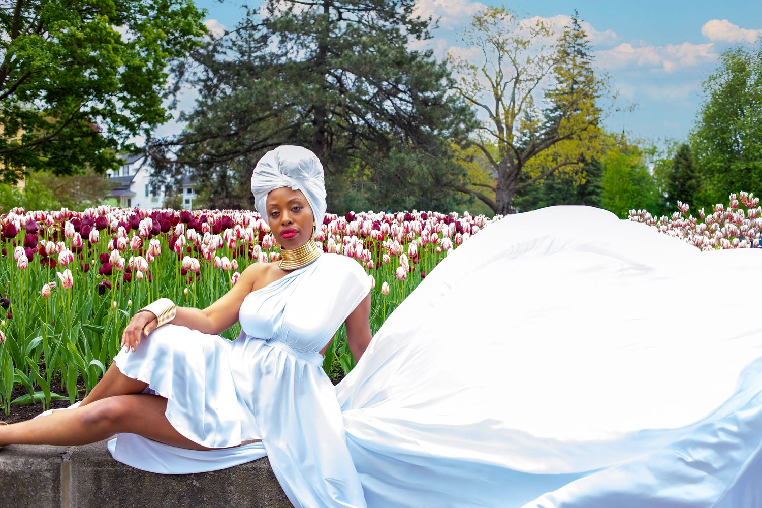 Woman in white dress and head wrap sits serenely among colorful tulip festival in a garden. Ottawa flying dress photography.