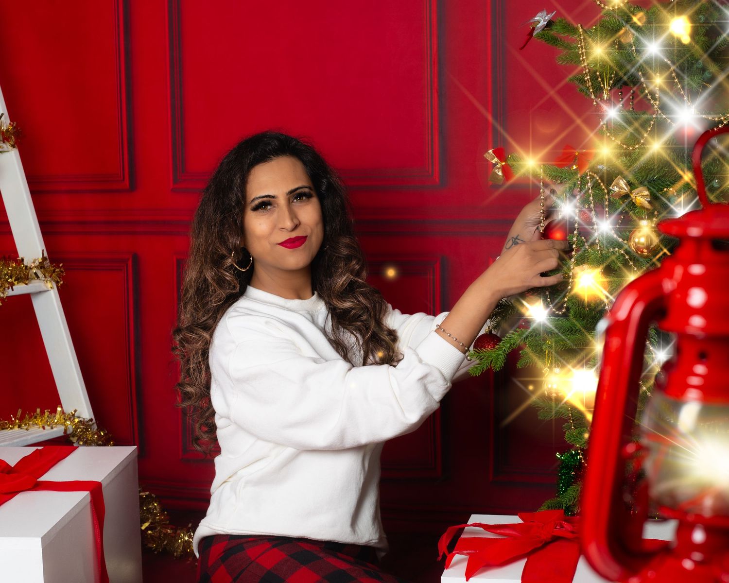 Woman in white sweater decorating a Christmas tree with lights, surrounded by gifts and red holiday decor.