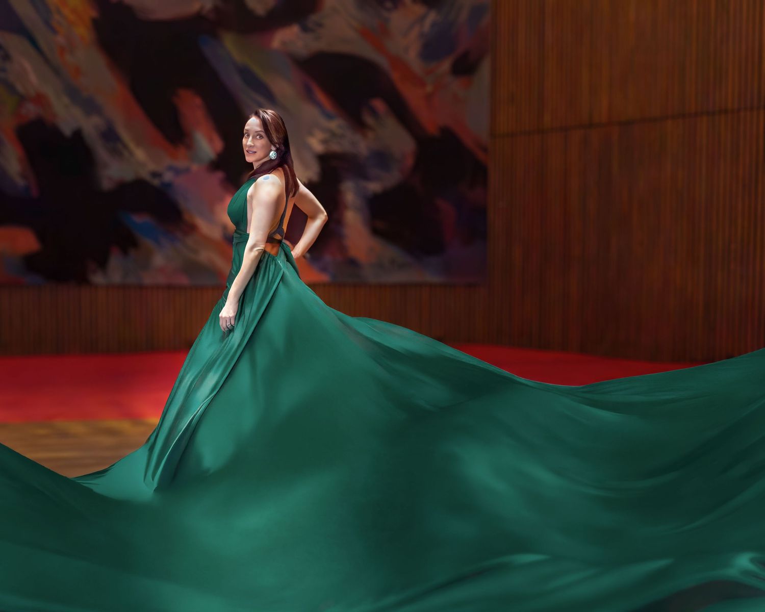 Woman in stunning emerald green flowing gown twirls in elegant interior with colorful artwork. Ottawa flying dress photography. NAC