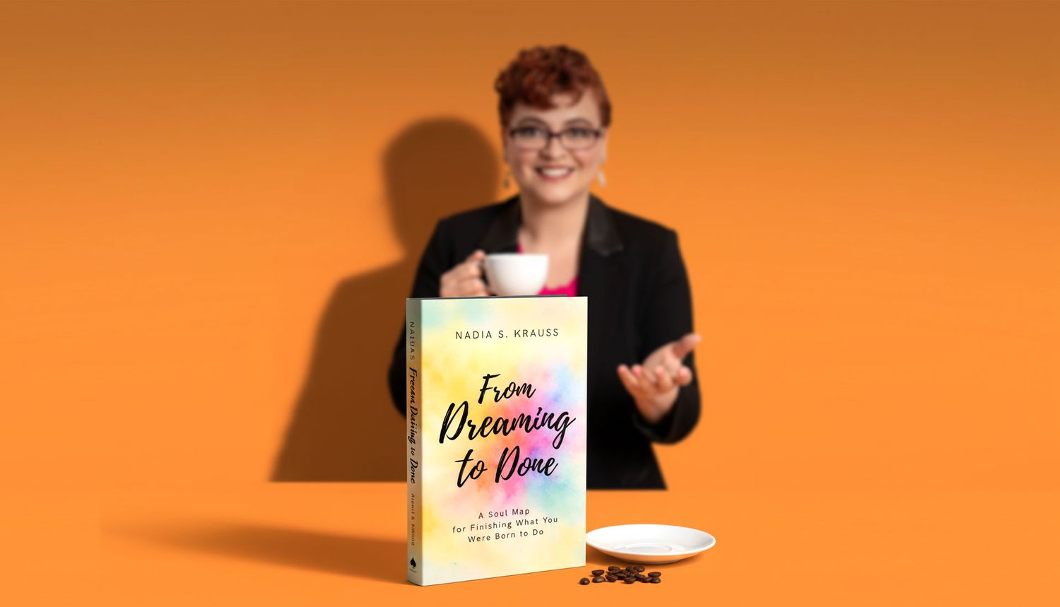 Author holding coffee cup beside From Dreaming to Done book on orange background.