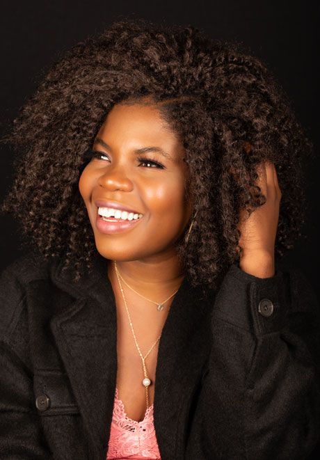 Joyful woman with natural curly hair smiling against dark studio background.