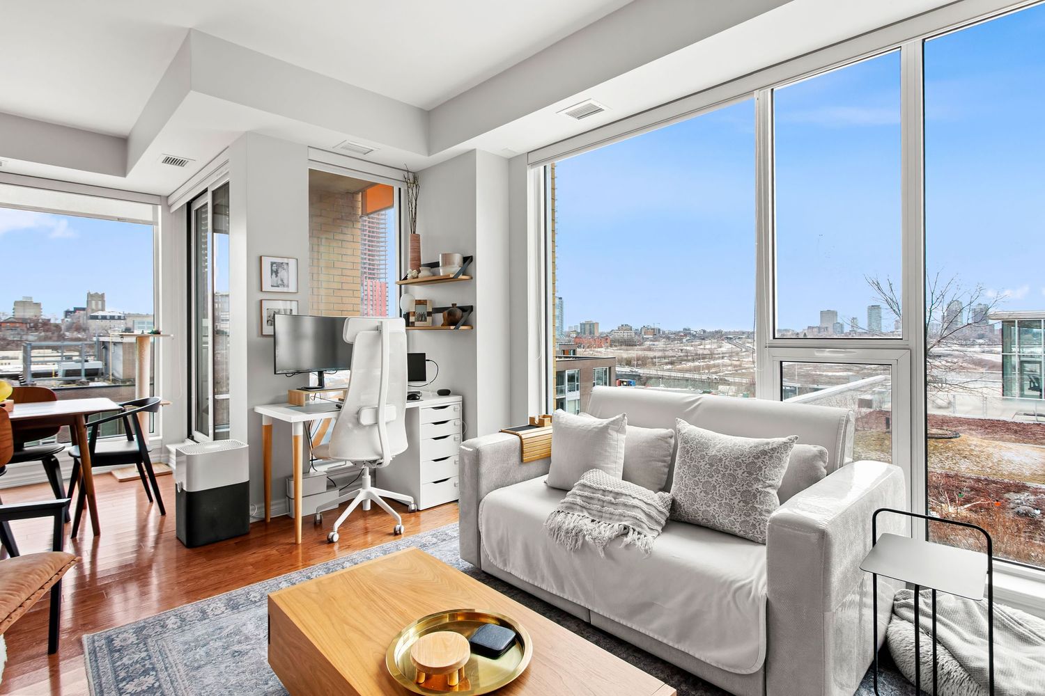 Professional real estate photography of Modern urban living room with floor-to-ceiling windows, city skyline views, and hardwood floors.