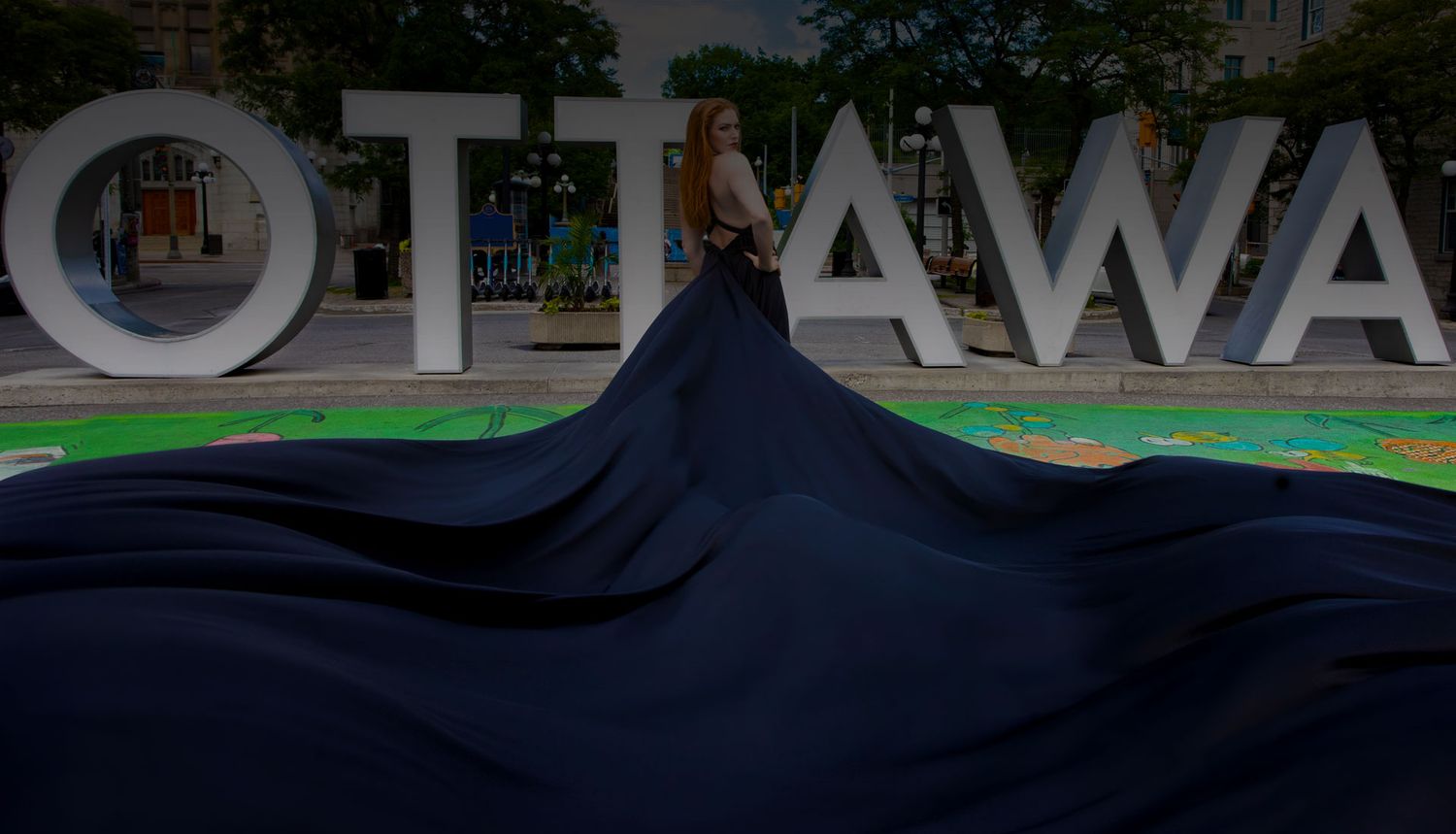Woman in dark flowing gown posing in front of large Ottawa city sign at dusk.