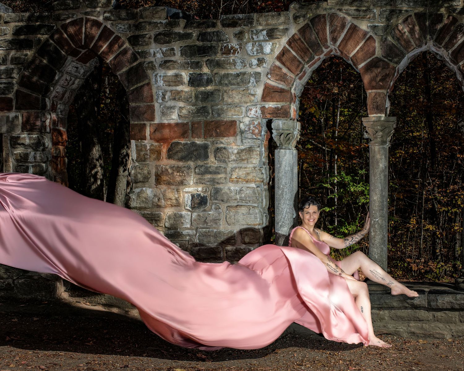 Woman in pink flowing fabric reclines against rustic stone arched ruins.  Ottawa flying dress photography. Mackenzie King estate