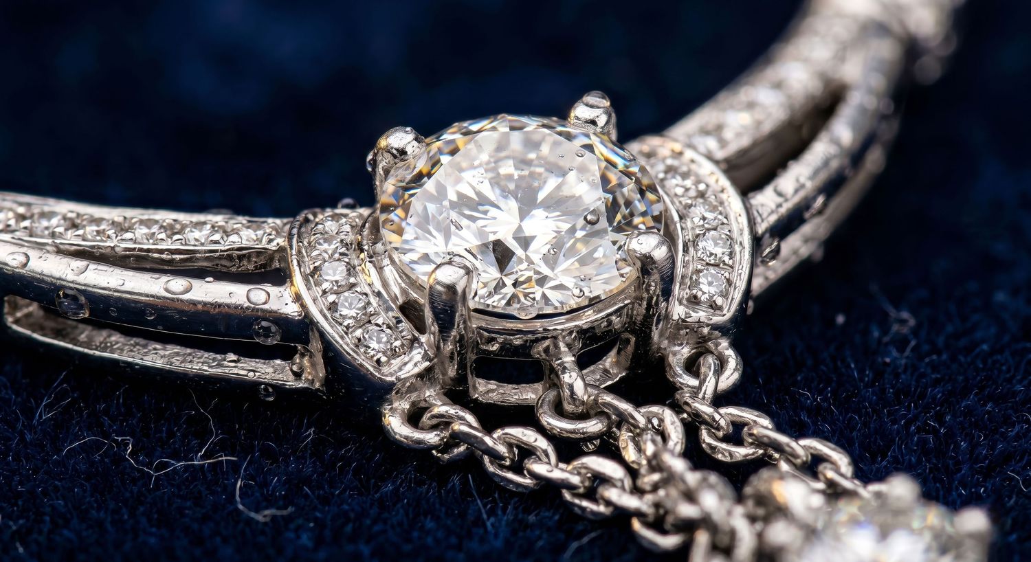 Close-up of vintage platinum diamond halo necklace with chain detail on dark blue velvet background.