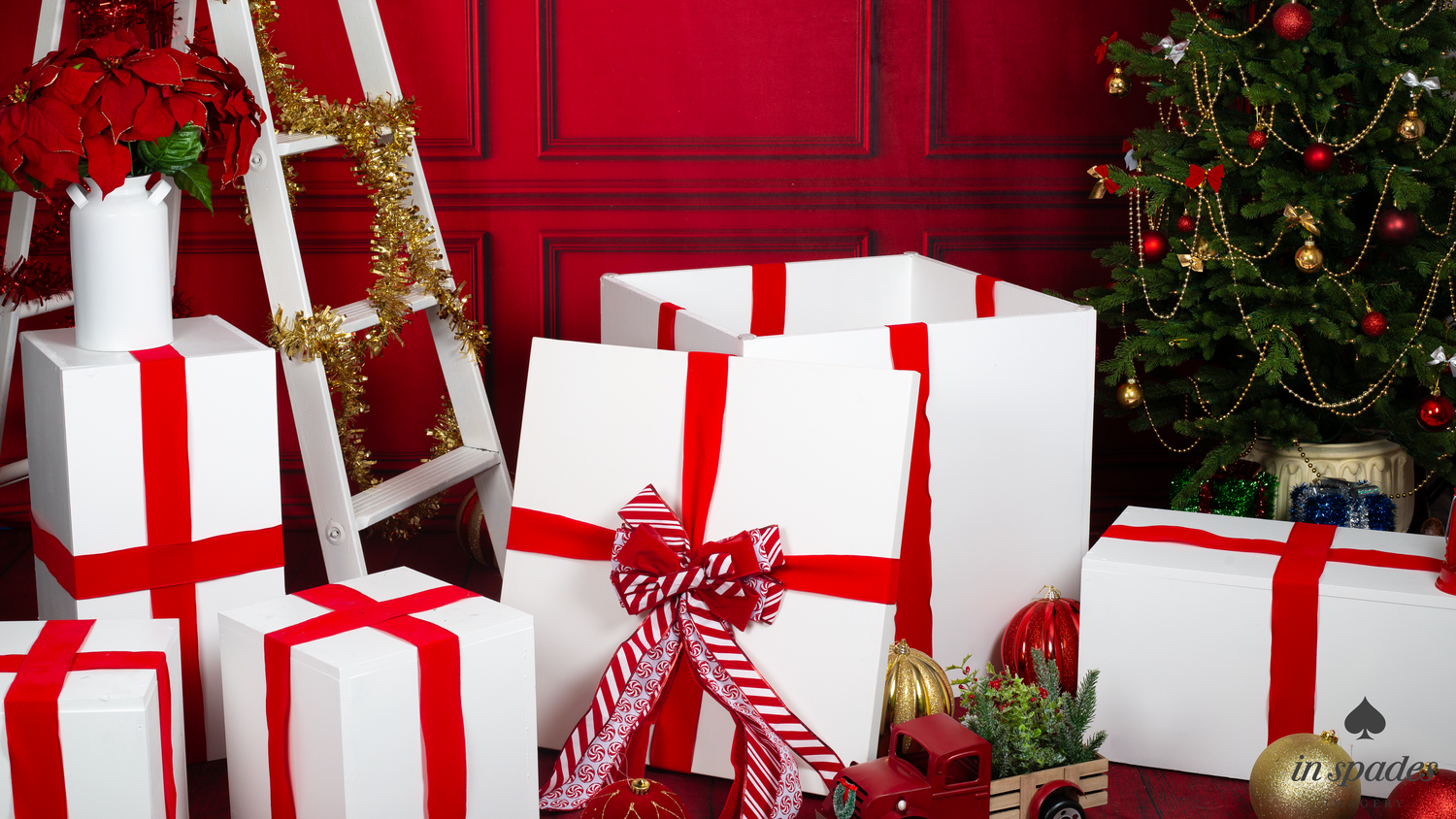 White gift boxes with red ribbons arranged near a decorated Christmas tree against a festive red wall.