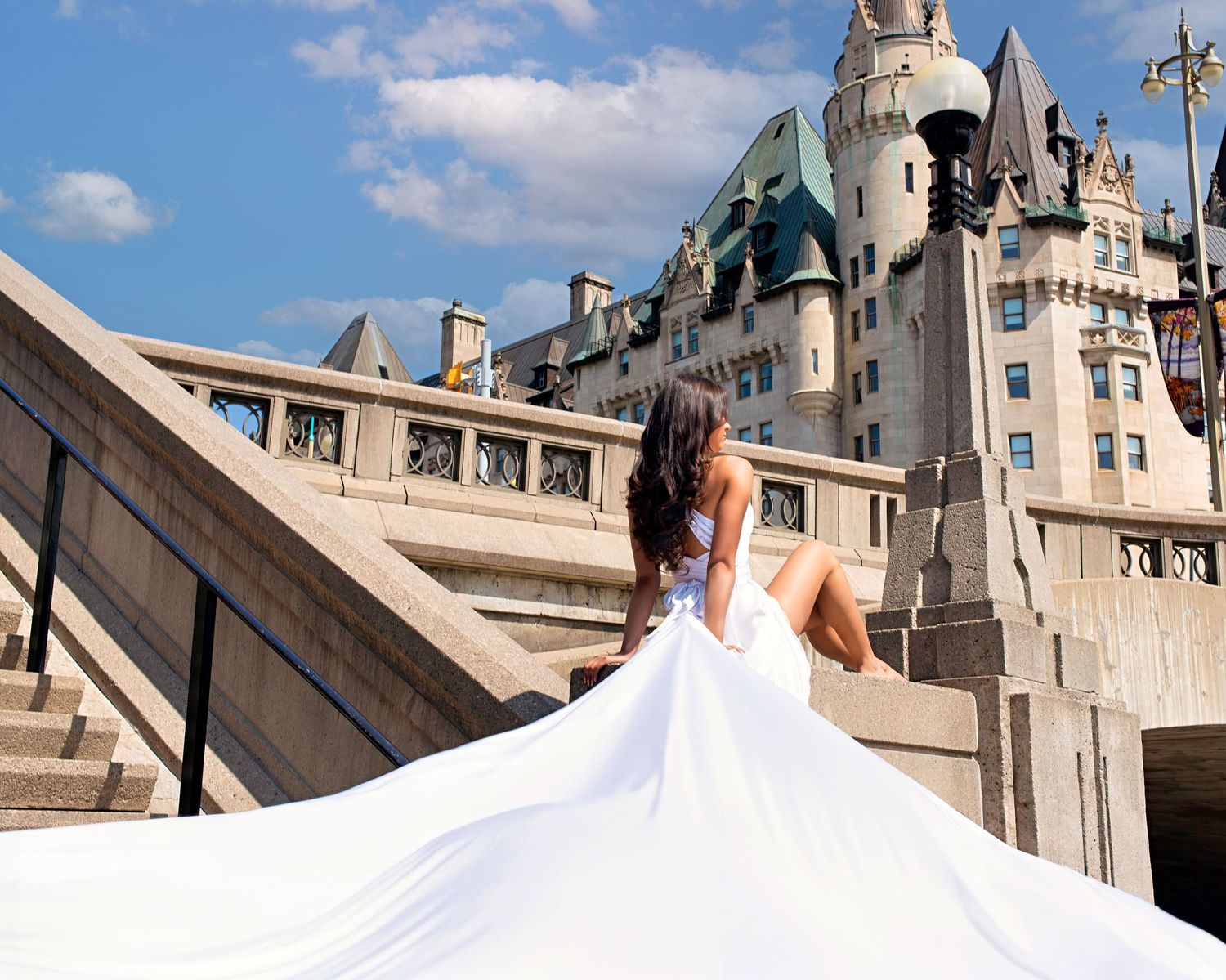 Woman in white flowing gown sits on stone steps before Chateau Laurier Ottawa. Ottawa flying dress luxury photography