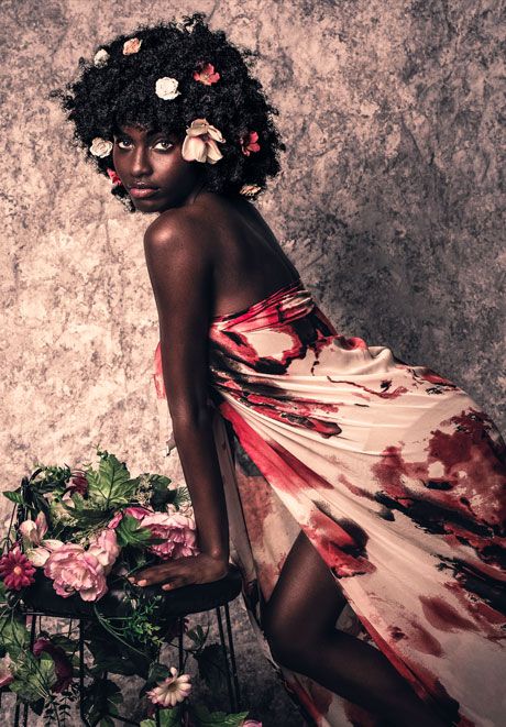Black woman in floral dress with flowers in natural hair in artistic studio portrait.