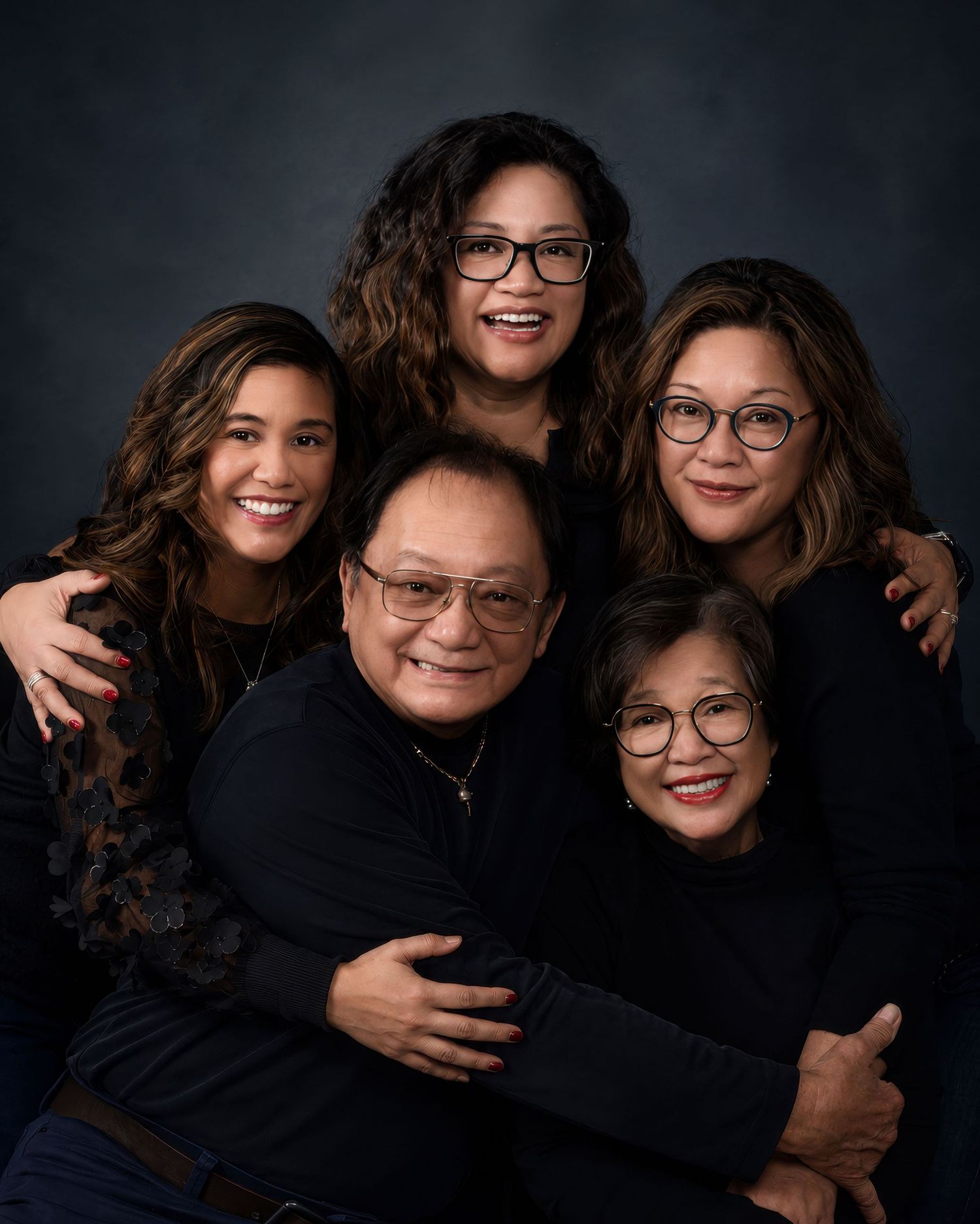 A loving Filipino family of five shares warm smiles in a close studio portrait with dark background. an Ottawa studio Family fine art
