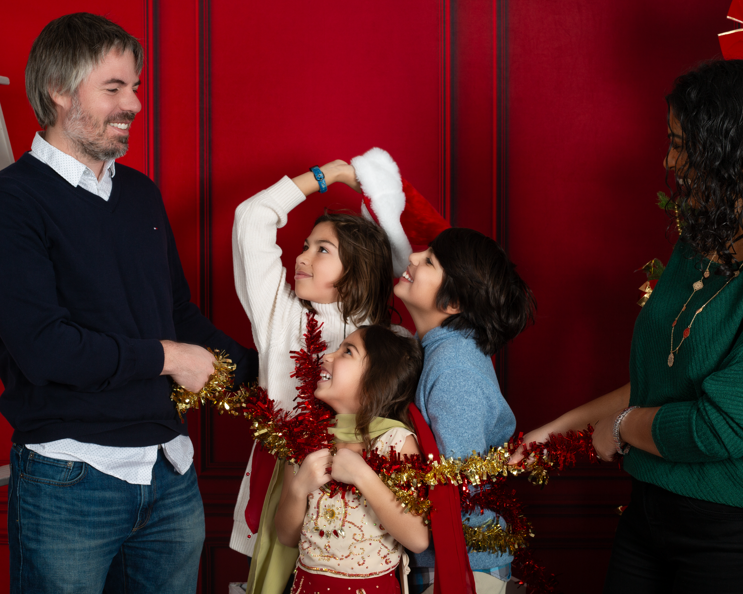 Family of four celebrating Christmas with gold tinsel garland against a festive red background.