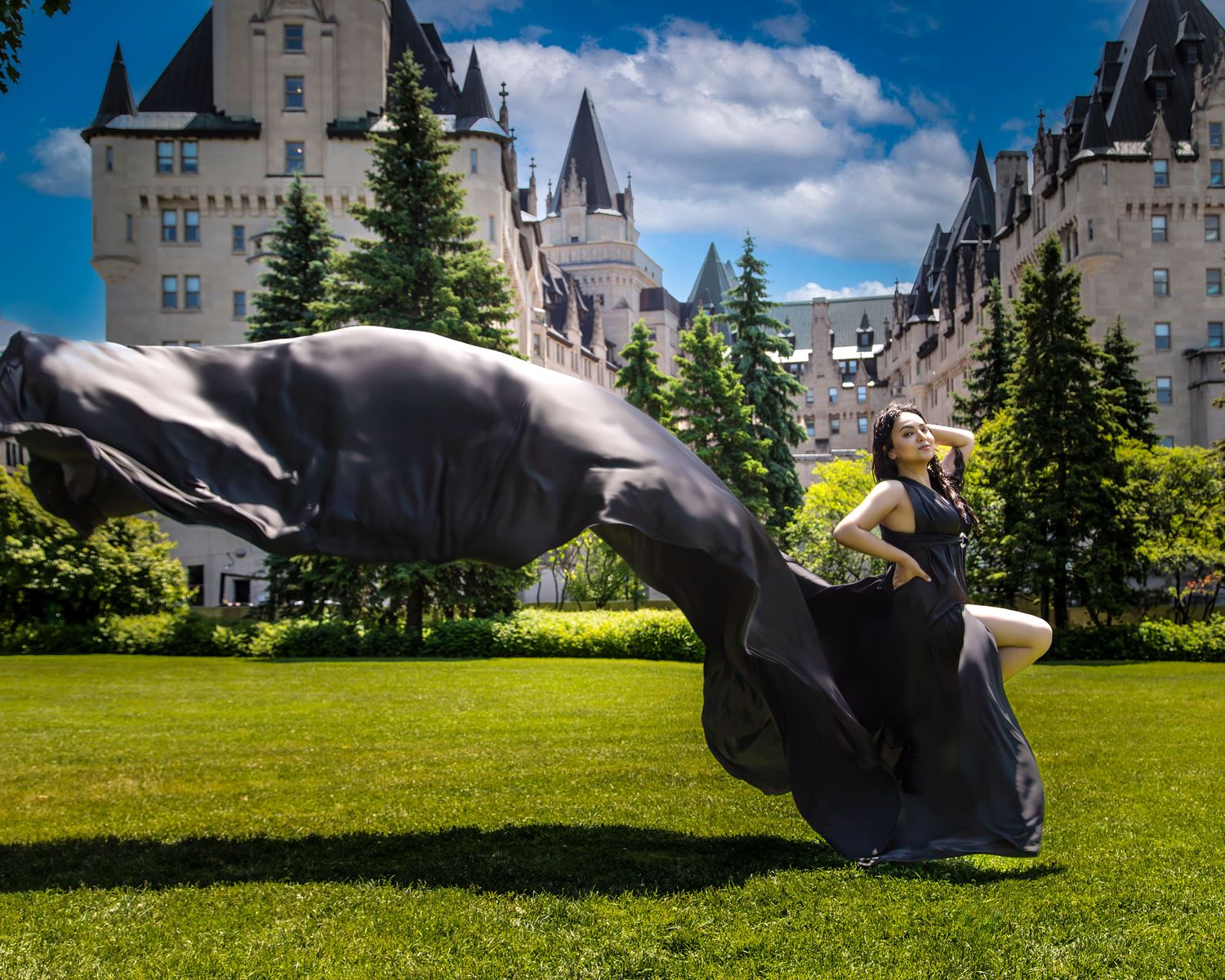Woman poses gracefully with billowing black fabric before the iconic Chateau Laurier hotel. Ottawa flying dress photography.
