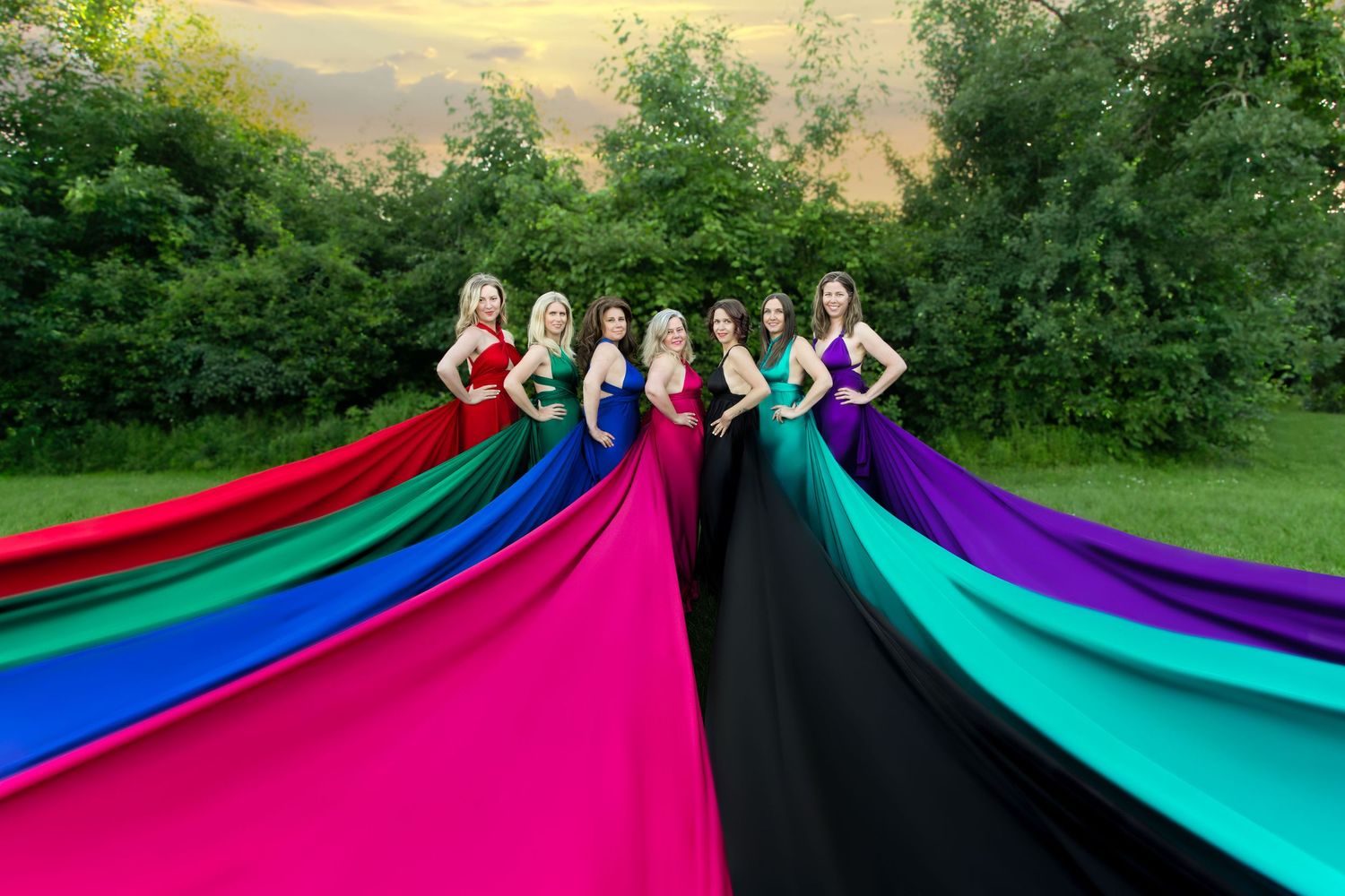 Group of women in colorful flowing gowns lined up outdoors creating rainbow of fabric trains. Ottawa flying dress photography. Findlay Creek
