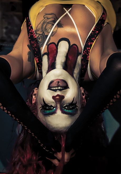 Dramatic upside-down portrait of woman with clown face paint, teal eye makeup, and tattoos.