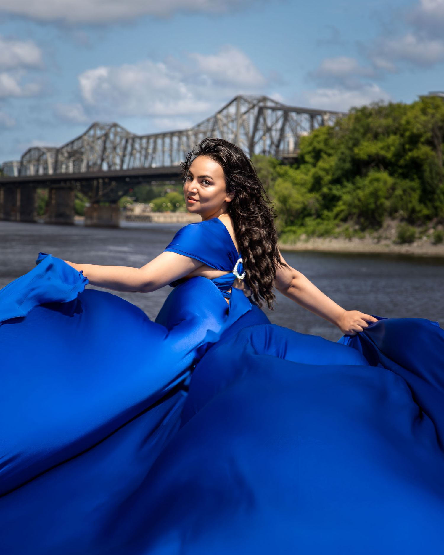 Woman in royal blue gown with flowing fabric poses by the Ottawa River and bridge. Ottawa flying dress photography.