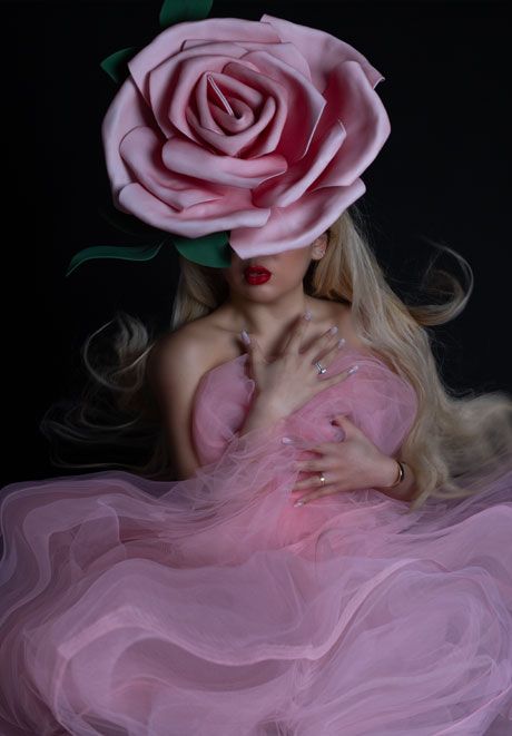 Surreal fashion portrait of woman in pink tulle gown with oversized pink rose covering her face.