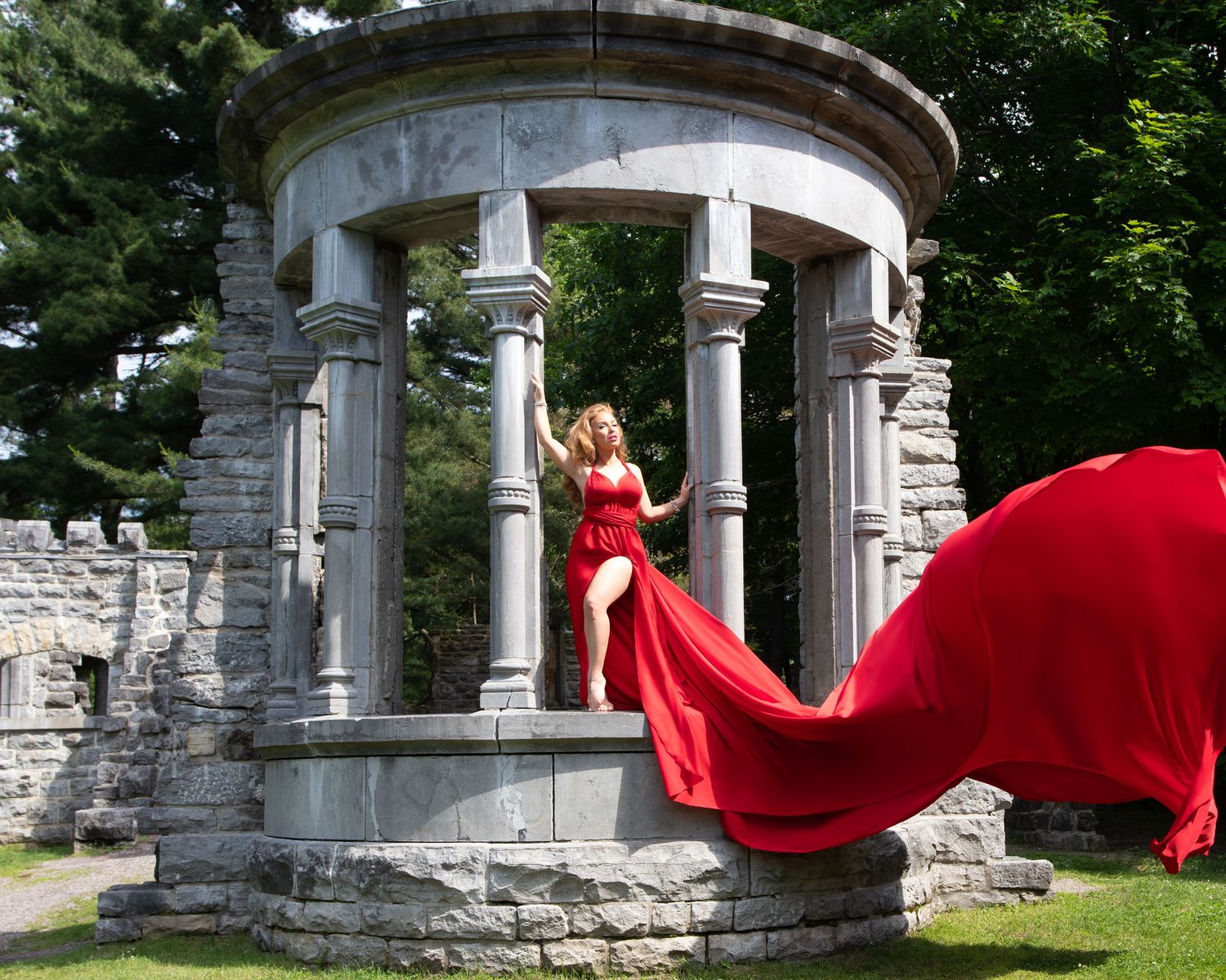 Woman in red flowing gown poses dramatically in stone rotunda ruins  Ottawa flying dress photography. Mackenzie King estate.