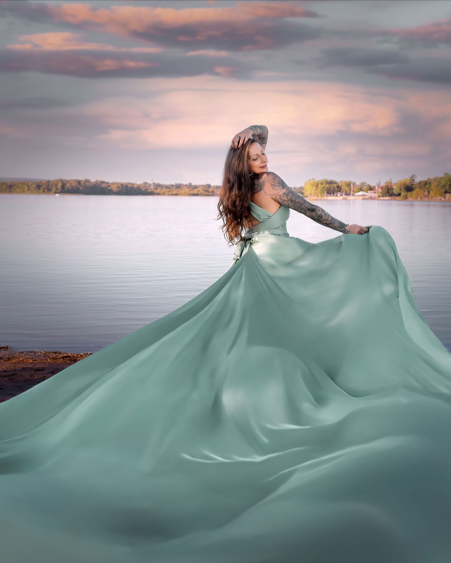 Woman in sage flowing gown stands by a serene lake under a dramatic sunset sky. Ottawa flying dress luxury photography. Britannia beach