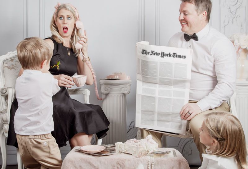 Family gathered around a table reading The New York Times in an elegant white room.