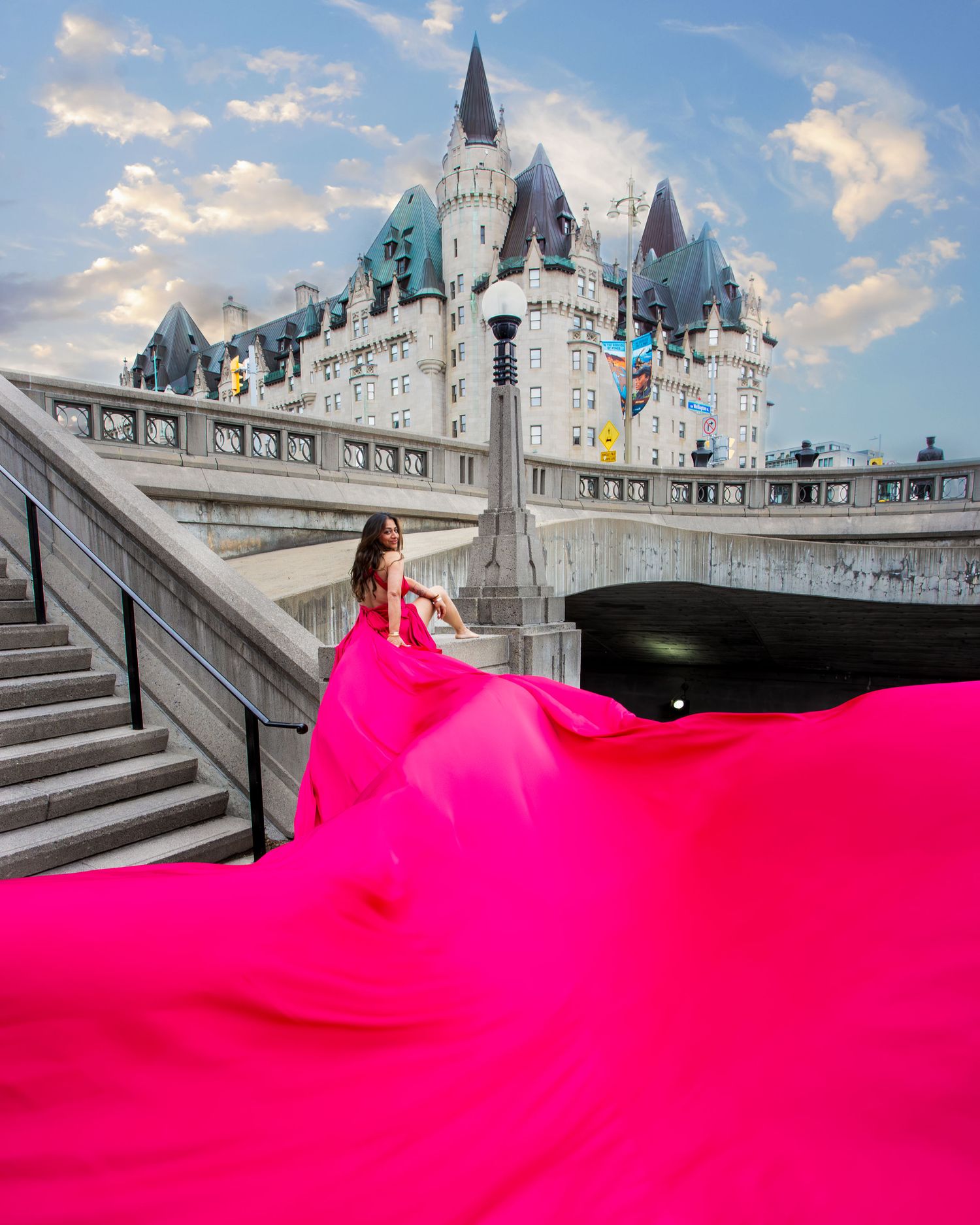 Woman in hot pink gown with dramatic flowing train on steps near castle-like building. Ottawa flying dress photography. Château Laurier
