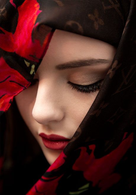 Woman with red lips and closed eyes wears floral Louis Vuitton headscarf with red flowers.