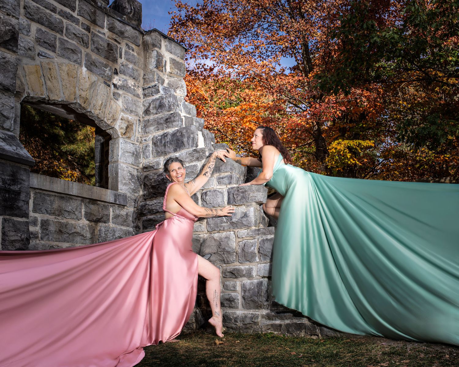 Two women in rose gold and sage gowns dance beside a stone castle wall in autumn. Ottawa flying dress photography. Mackenzie King estate