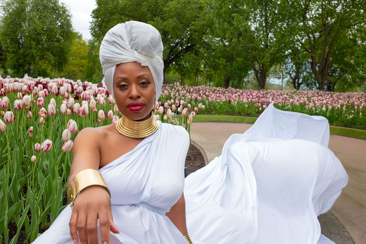 Regal woman in white dress gold jewelry and head wrap poses in tulip garden festival. Ottawa flying dress luxury photography