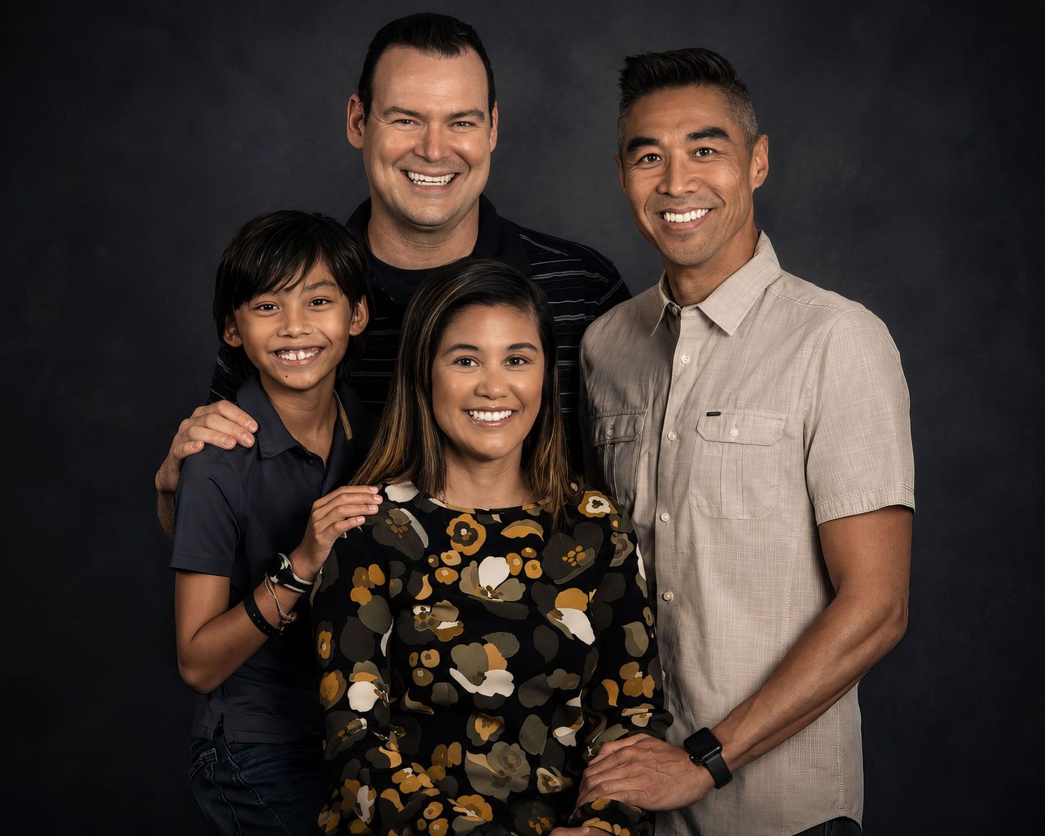 A happy family of four smiles together in a warm professional studio portrait with dark background an Ottawa studio Family fine art portrait