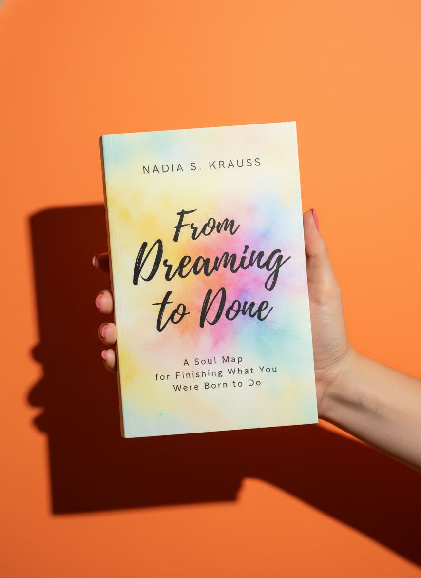 Hand holding From Dreaming to Done book by Nadia S. Krauss against orange background.