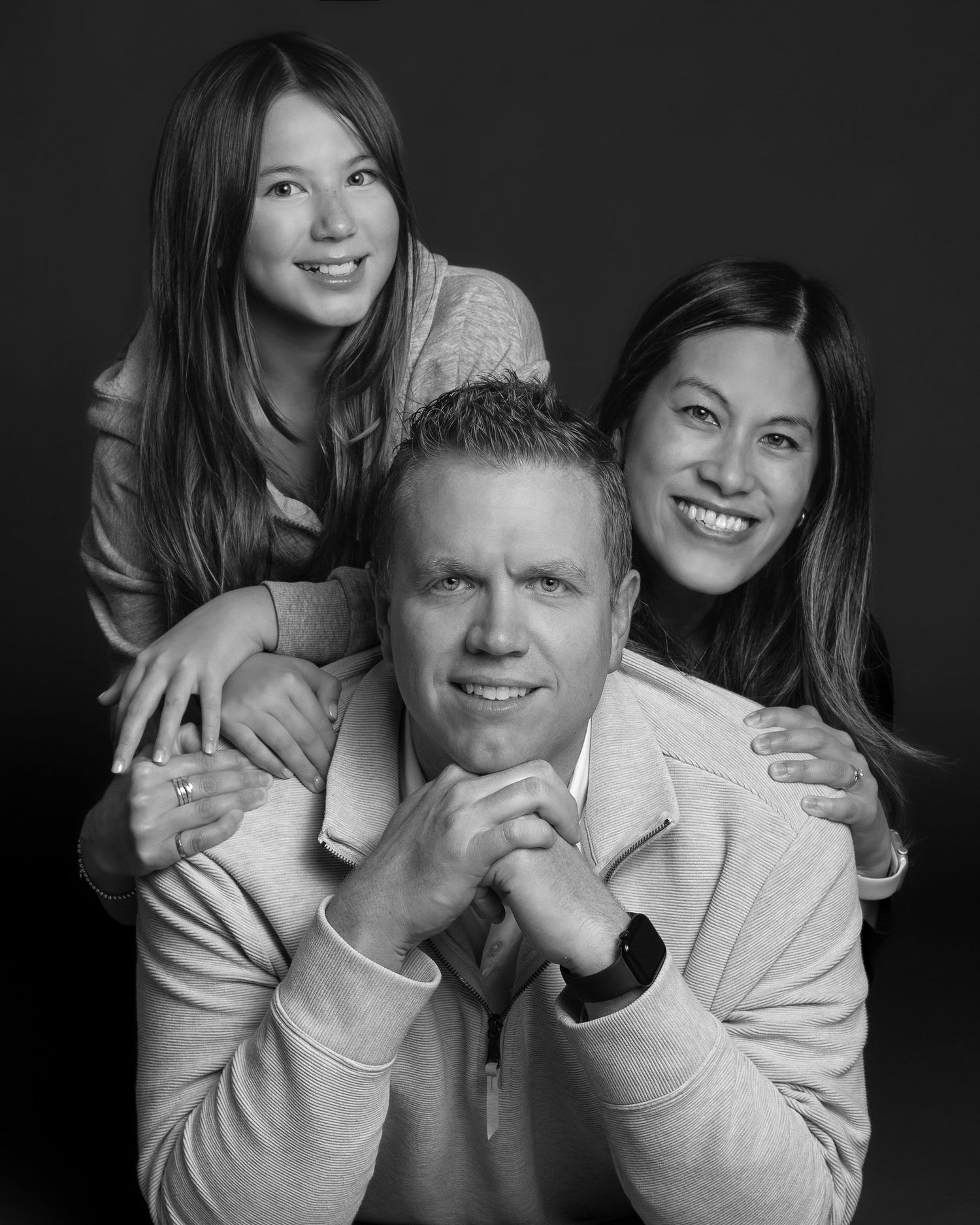 A black and white studio portrait of a smiling family of three posed in a playful stacked arrangement. an Ottawa studio Family portrait