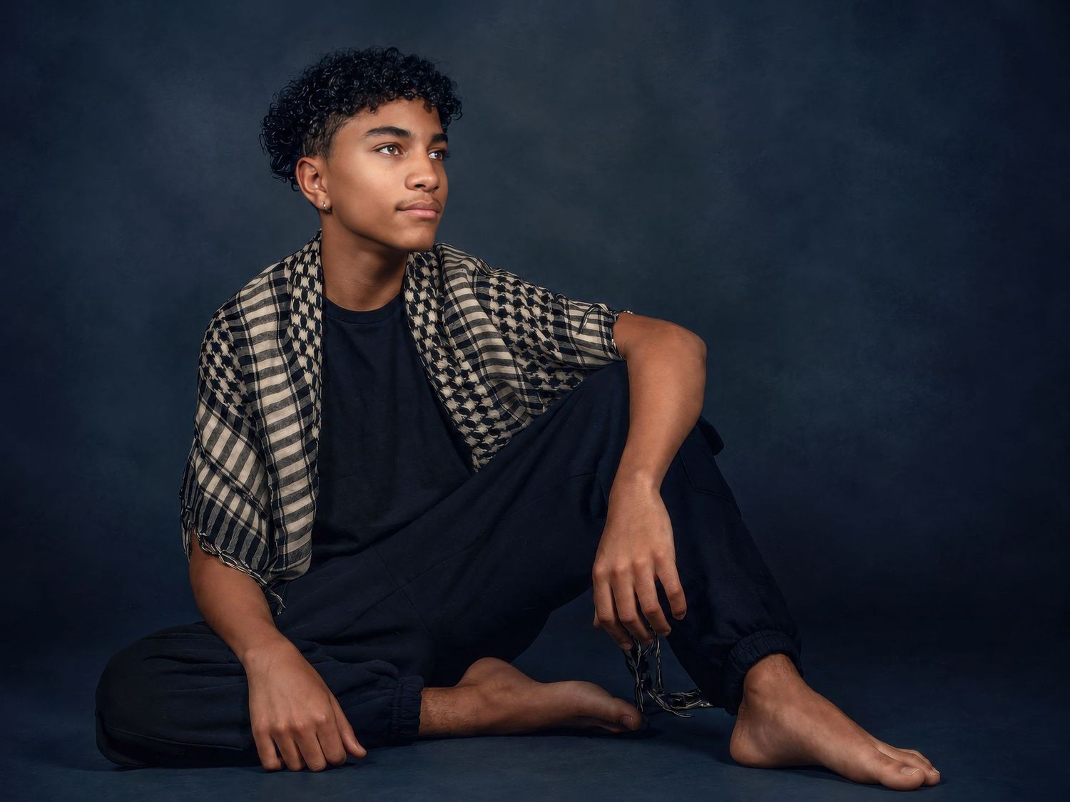 A teenage boy with curly hair sits barefoot in a stylish studio portrait. Ottawa model and actor