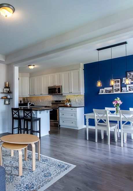 Open-concept kitchen and dining area with white cabinets, bold blue accent wall, and hardwood floors.