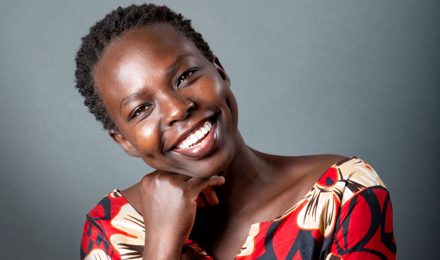 Smiling African woman in colorful red floral top against gray background portrait.