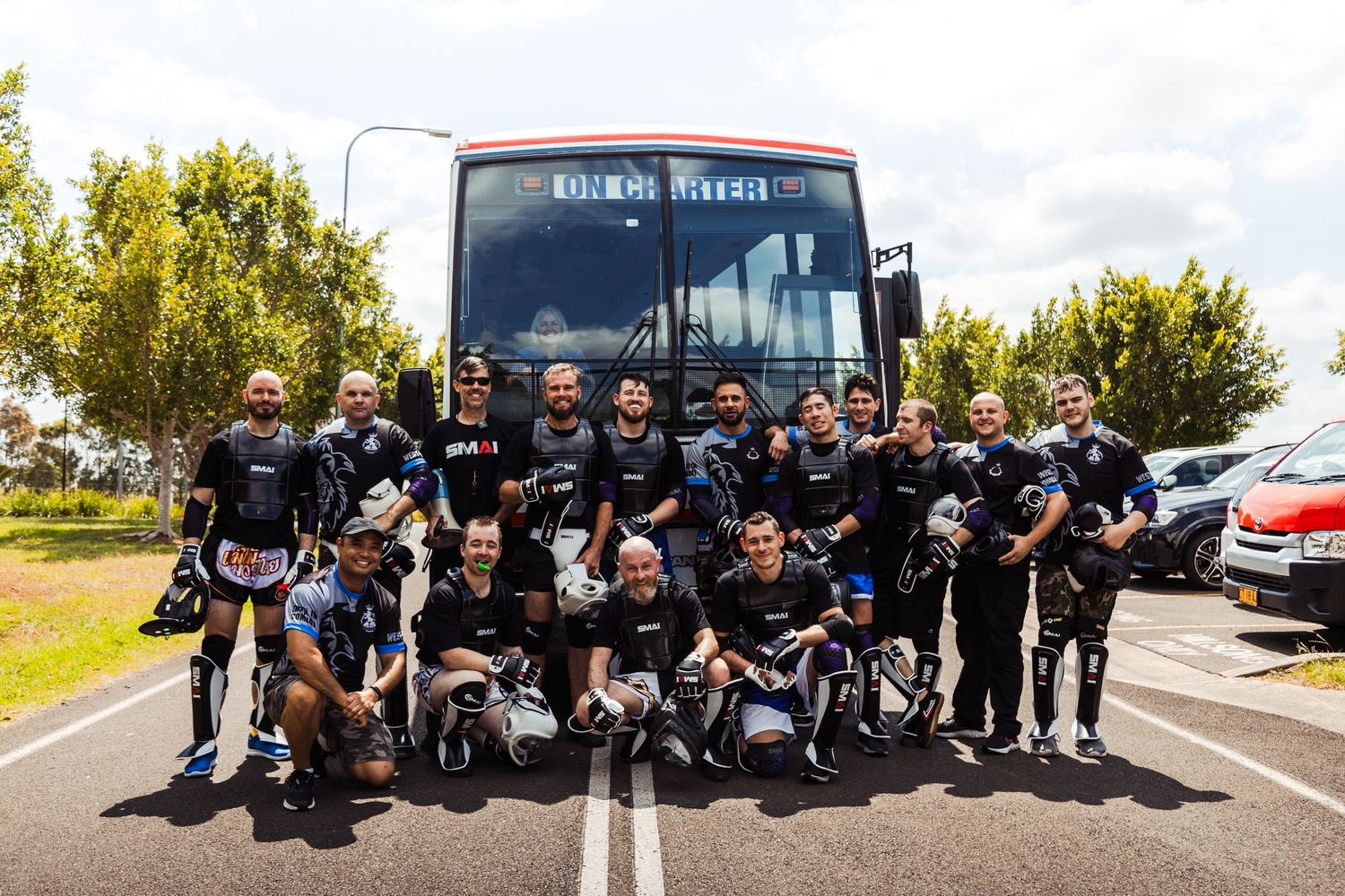 Main stars and co-stars of the Ultimate Self Defence Championship season 1 posing in front of a bus for a group photo in their fight gear.