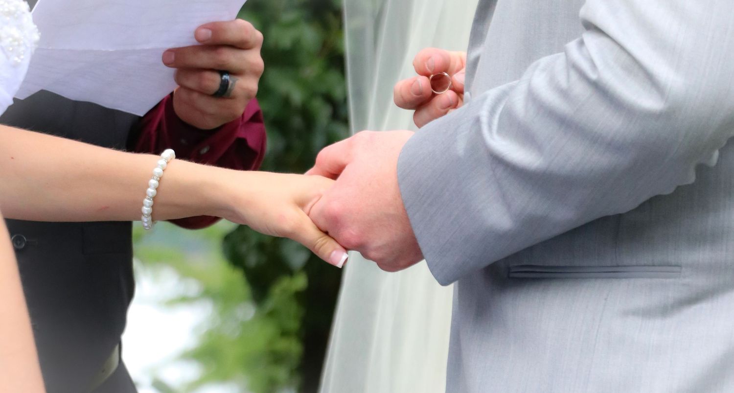 Close-up of hands exchanging wedding rings during ceremony.