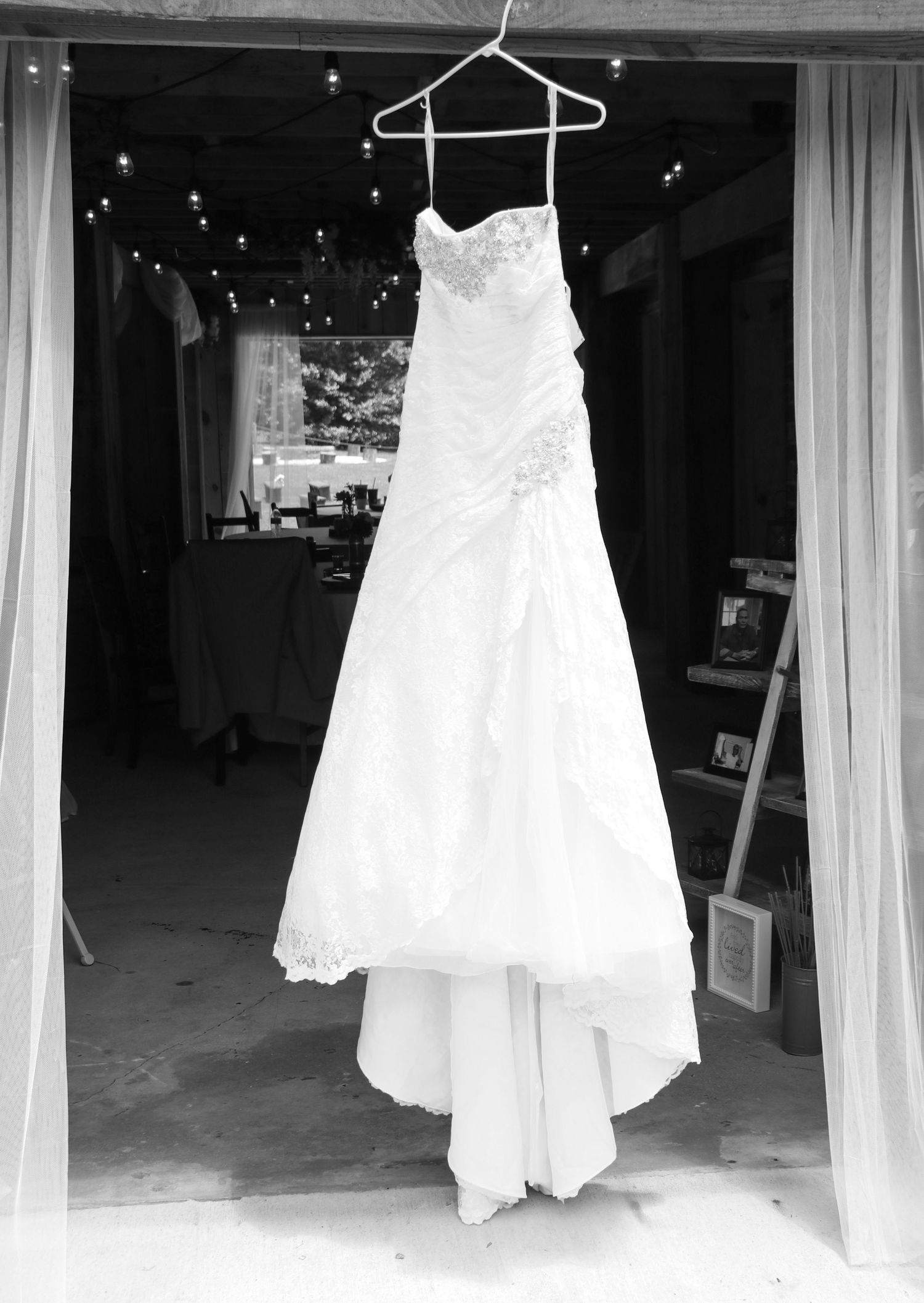 An elegant white lace wedding dress hangs on display with twinkling lights in the background.