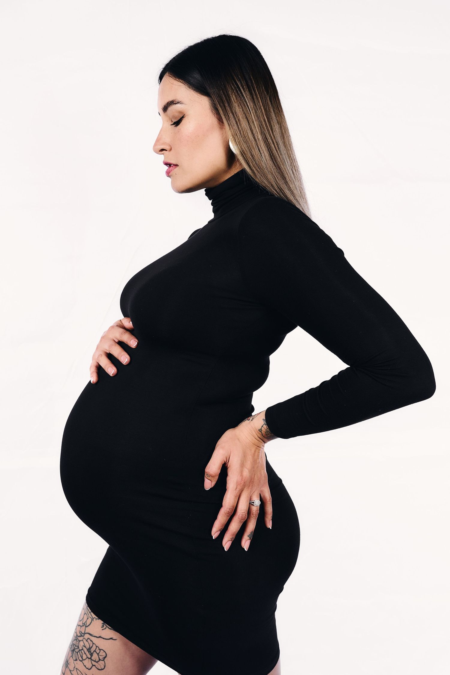 Maternity photos showing a pregnant belly in a black turtleneck against white background.