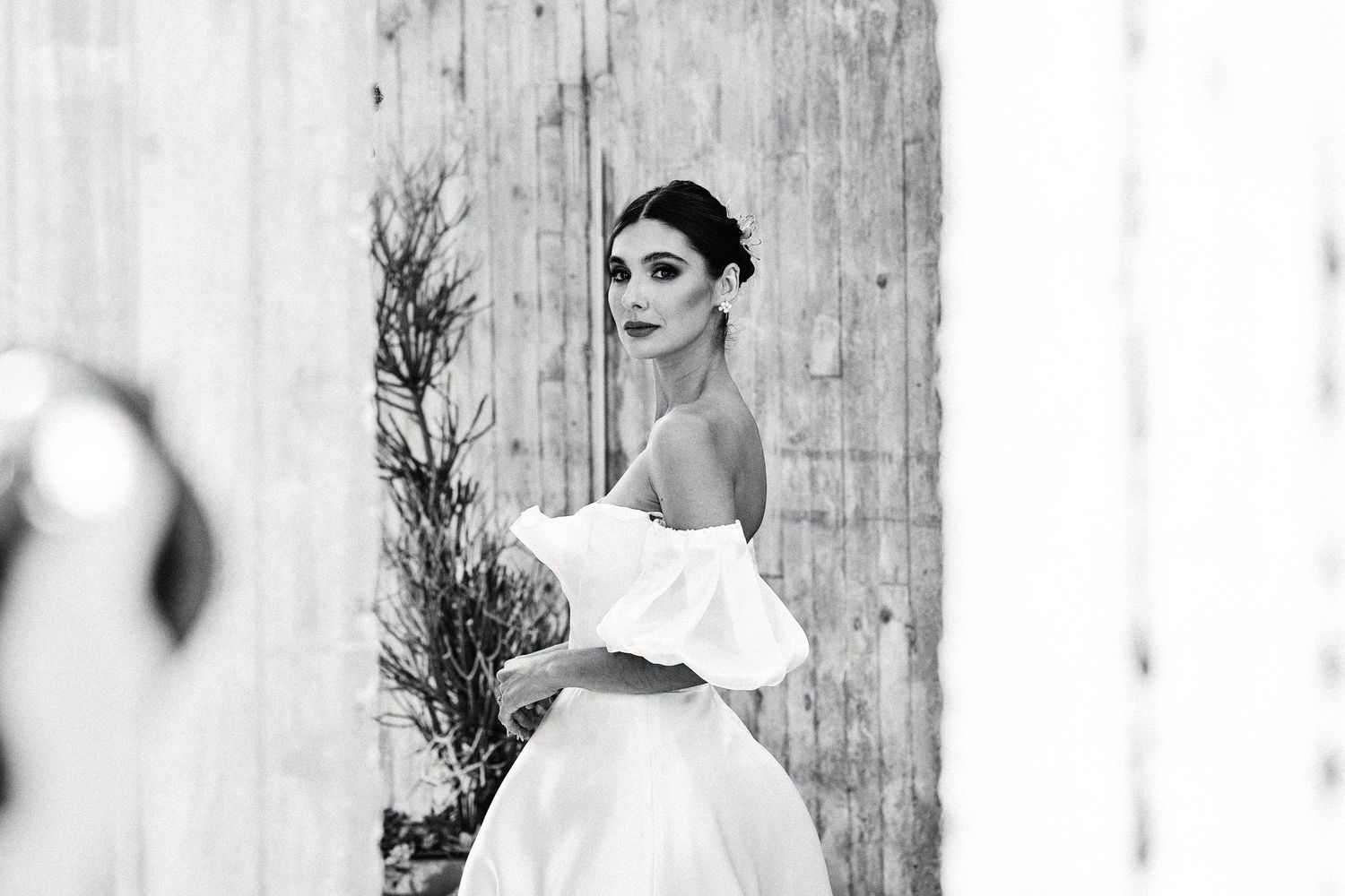 Black and white bridal portrait against rustic wooden wall with dramatic lighting.