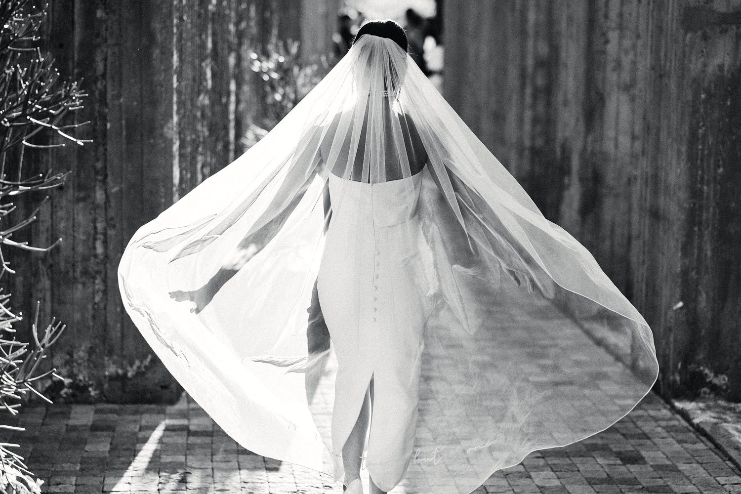 Bride twirling in a white wedding dress against a rustic wooden backdrop.