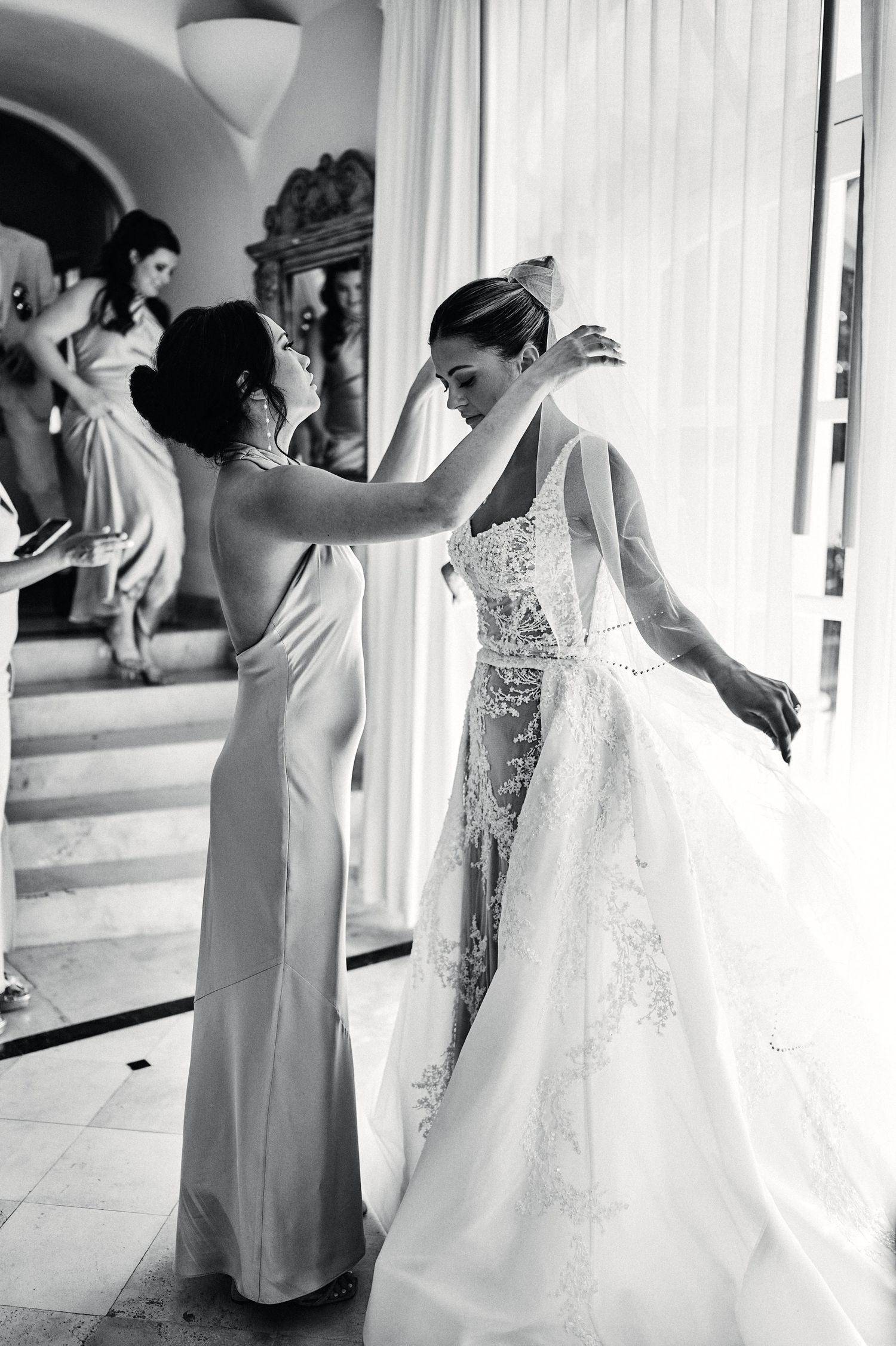 Black and white photo of wedding dress fitting with intricate lace details.