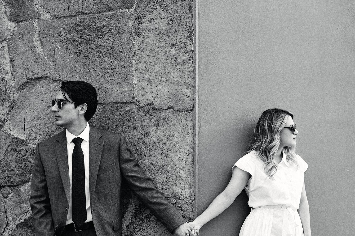 Black and white engagement portraits against textured stone wall background.