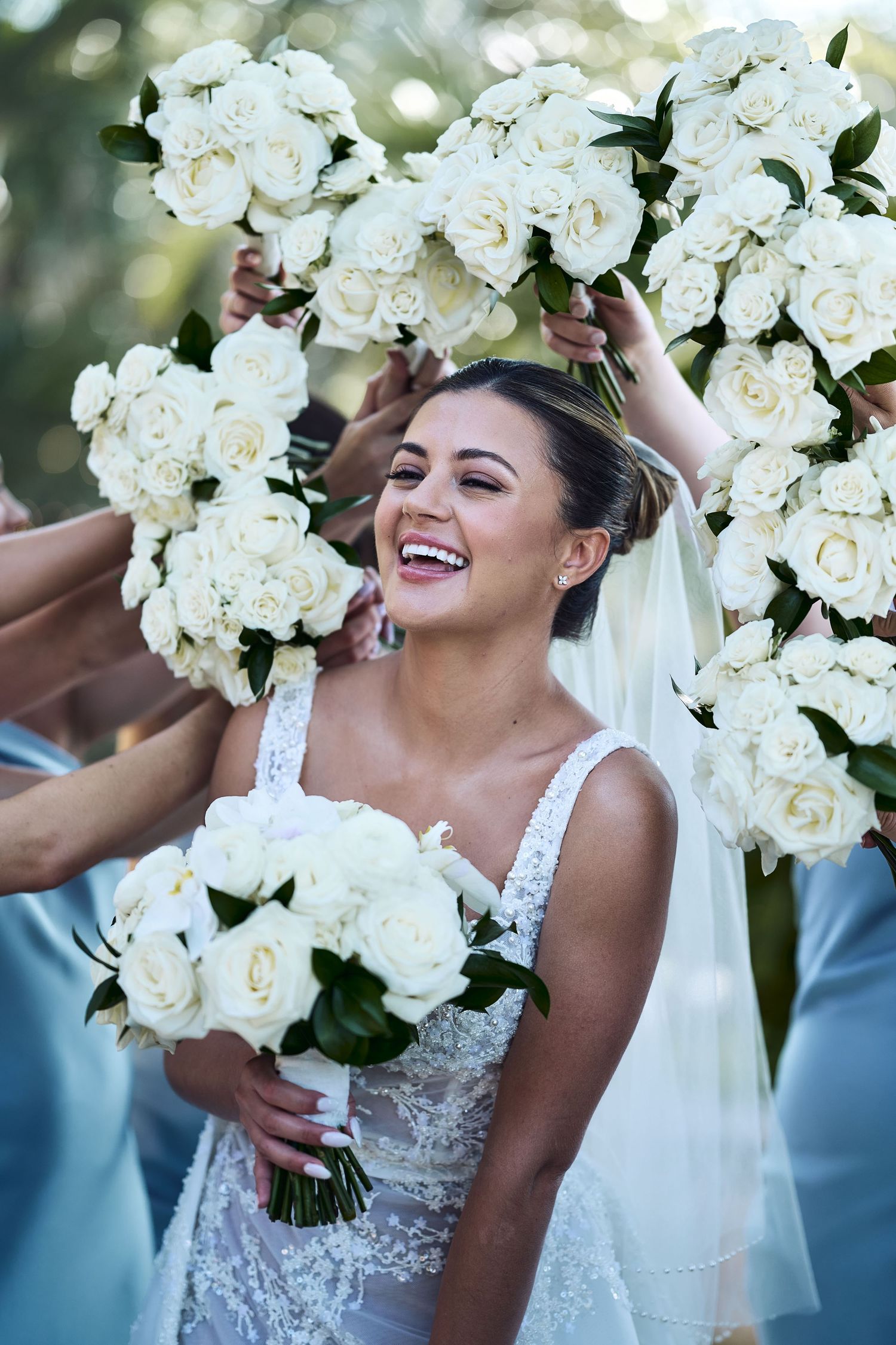 A joyful bride holds a stunning white rose bouquet while wearing a lace wedding dress and veil.