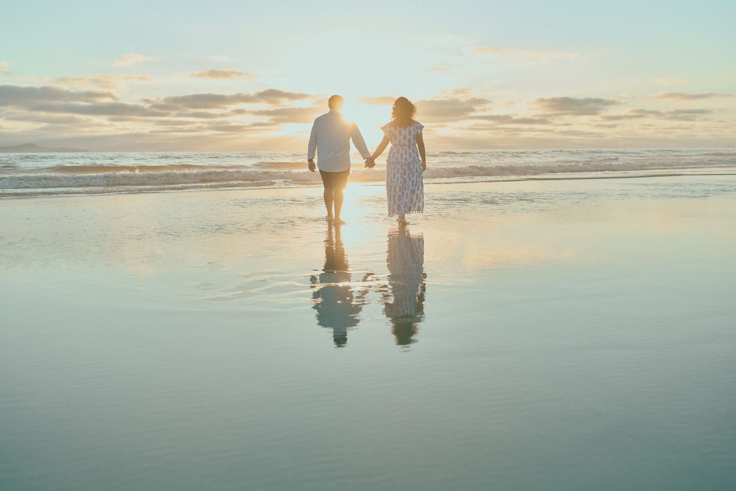 Romantic sunset beach wedding photo with couple silhouetted against pastel sky.