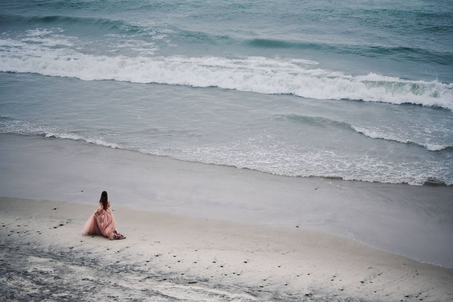 Distant figures on a serene beach with rolling waves and overcast sky.