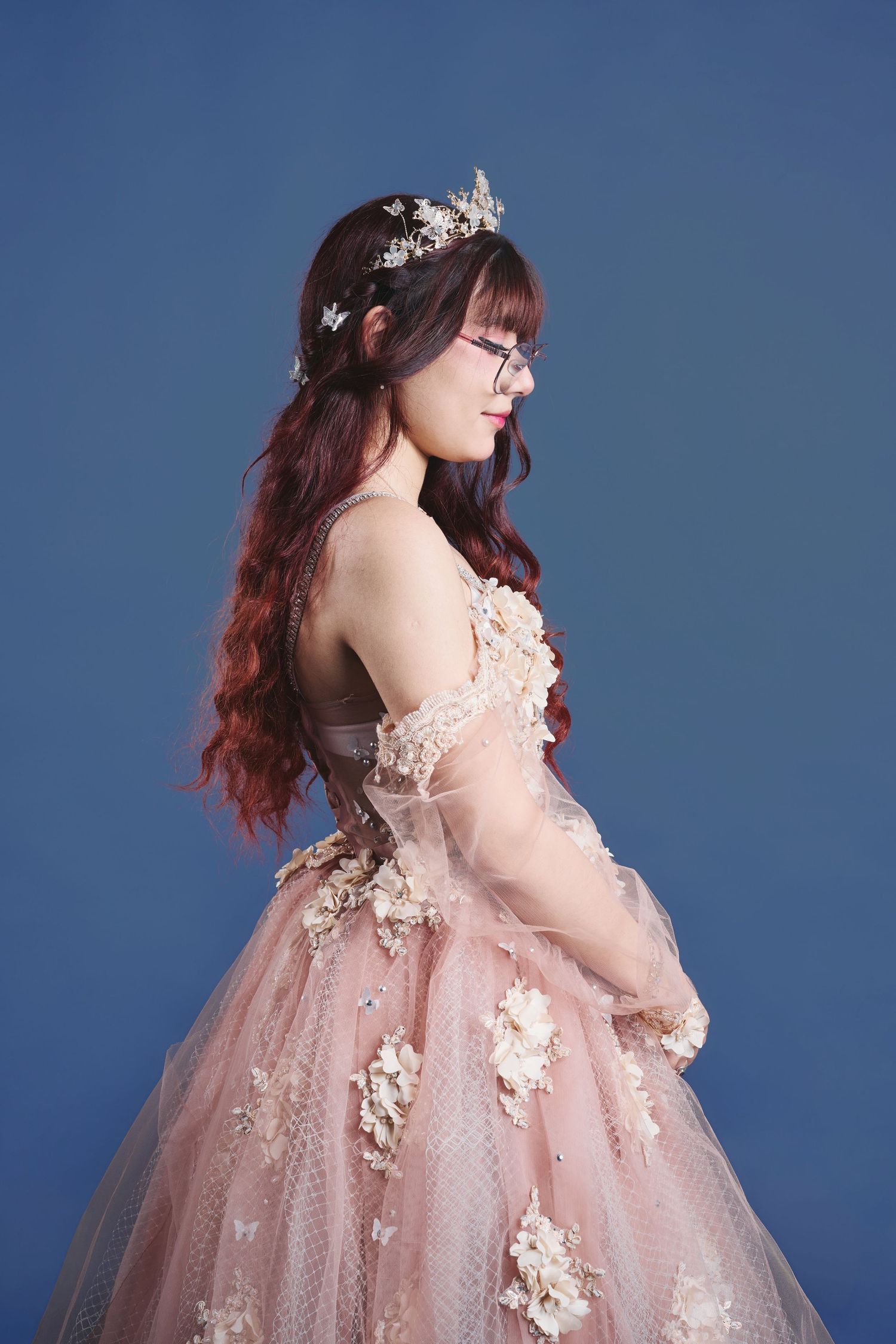 Romantic pink tulle gown with floral details photographed against blue backdrop.