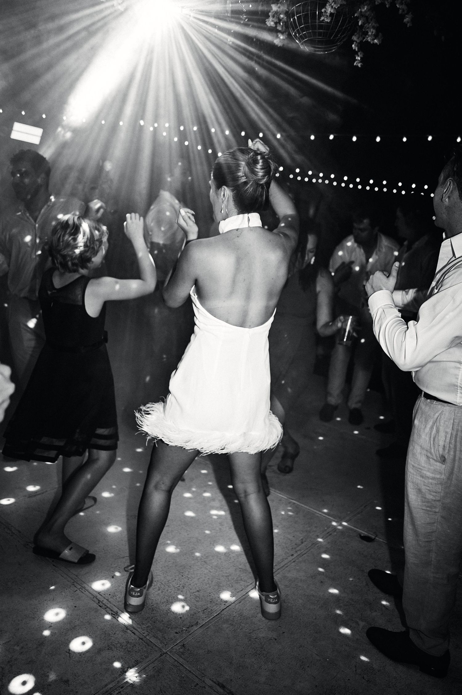People dancing under dramatic lighting and string lights at a nighttime party or celebration.