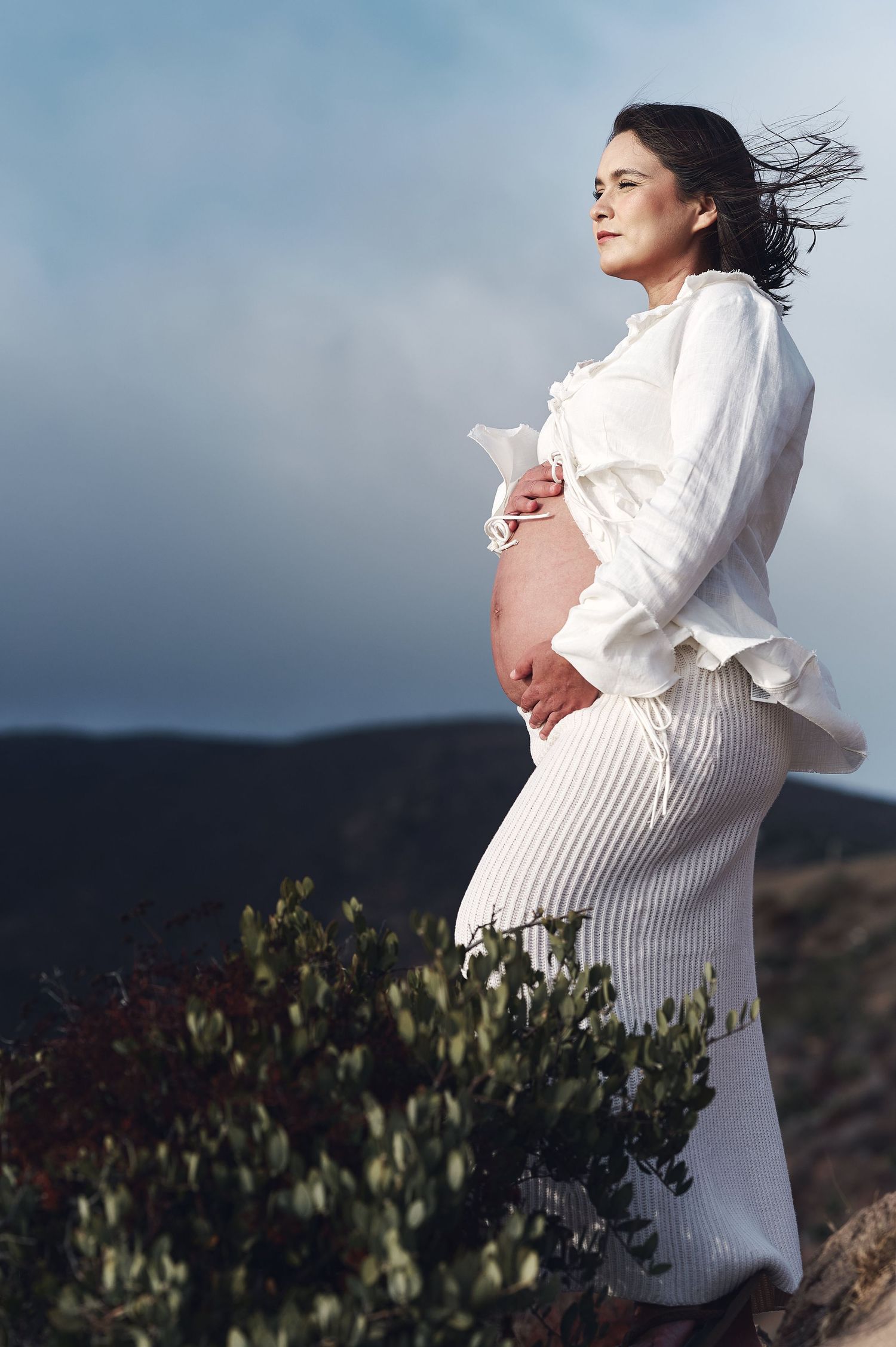 Serene maternity photo with flowing dress against mountain landscape.