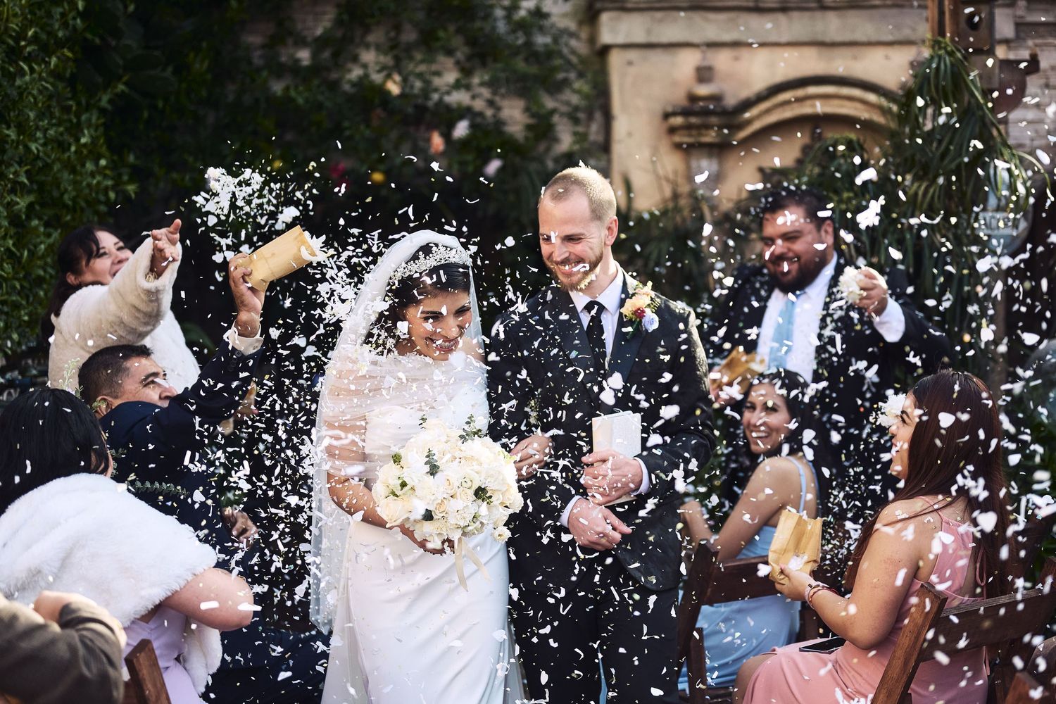 Wedding celebration with guests throwing white confetti in joyful celebration.