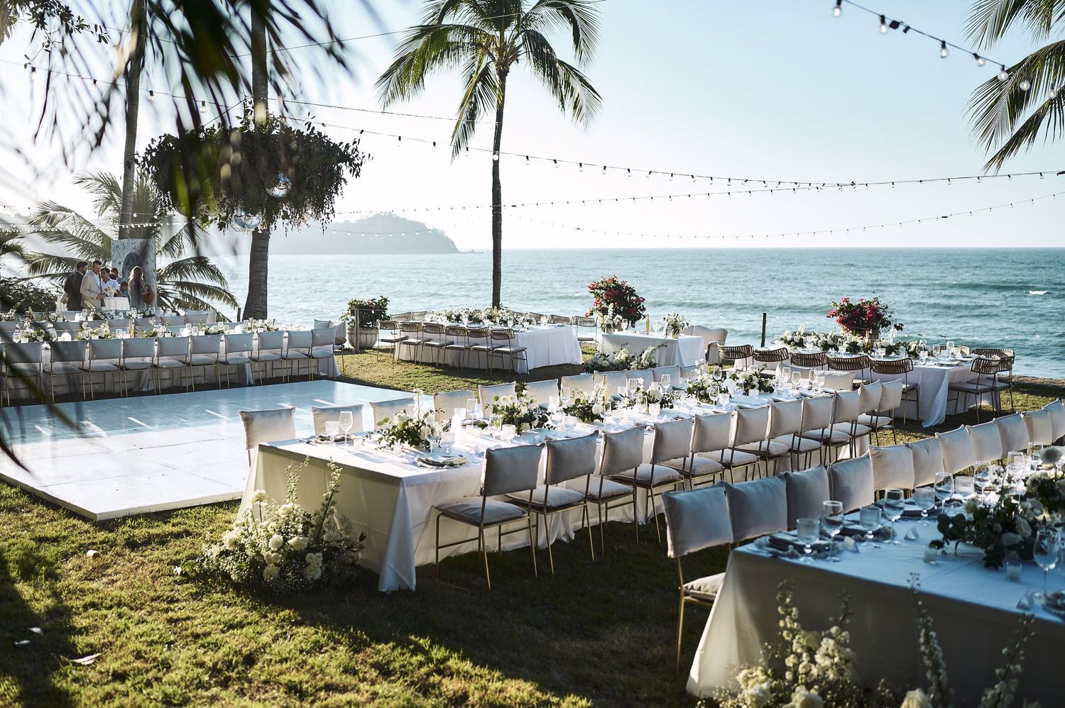 Beachside wedding reception setup with elegant white tables under palm trees.