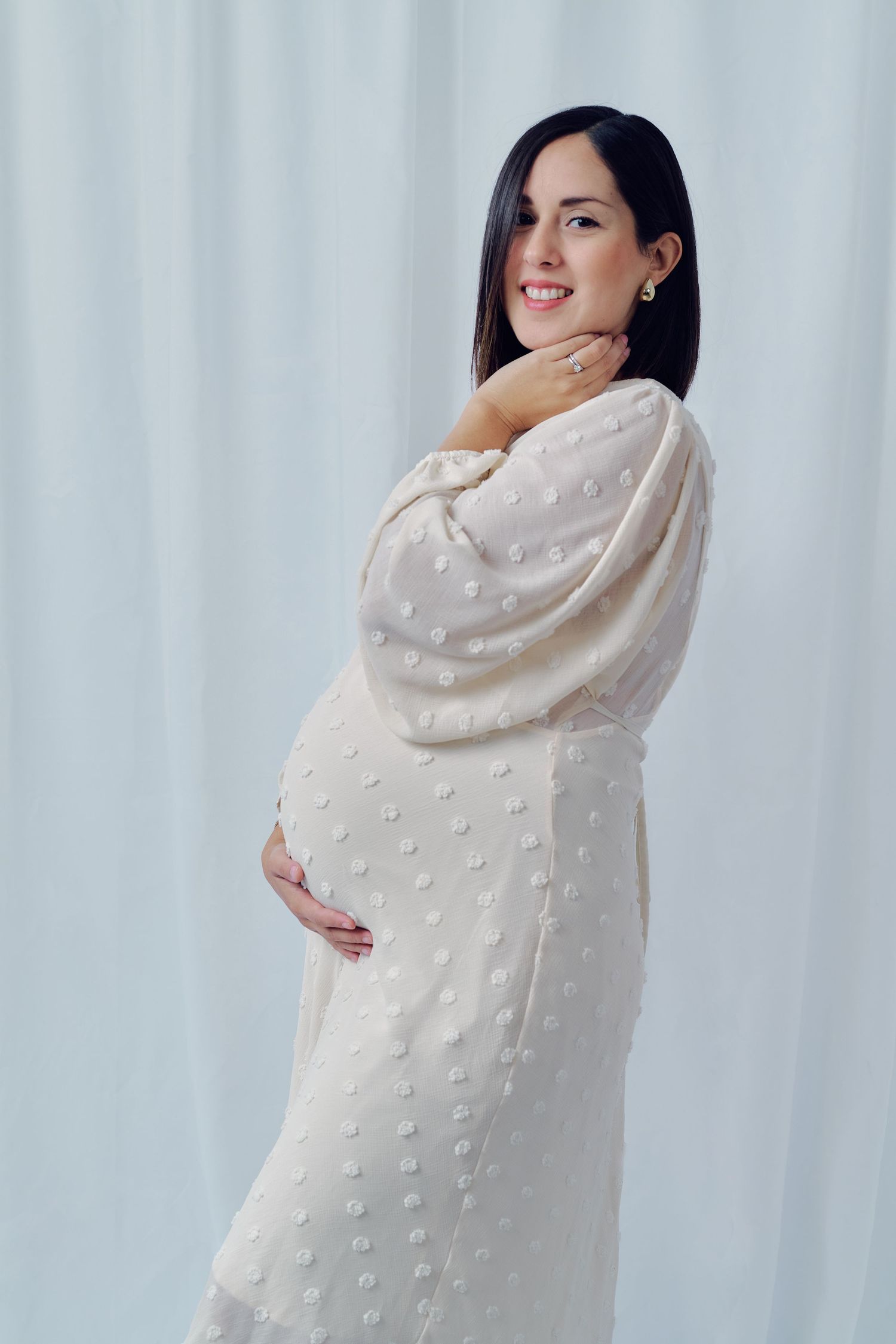Studio maternity portrait featuring a white textured dress against a light background.